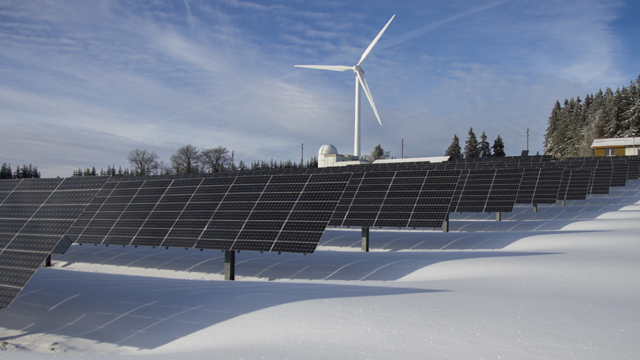 Solar panels with a wind turbine in the background in a snowy landscape