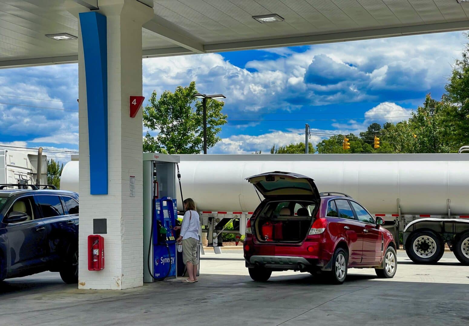 Woman pumps gas while an oil truck brings gas to refill tanks at a gas station.